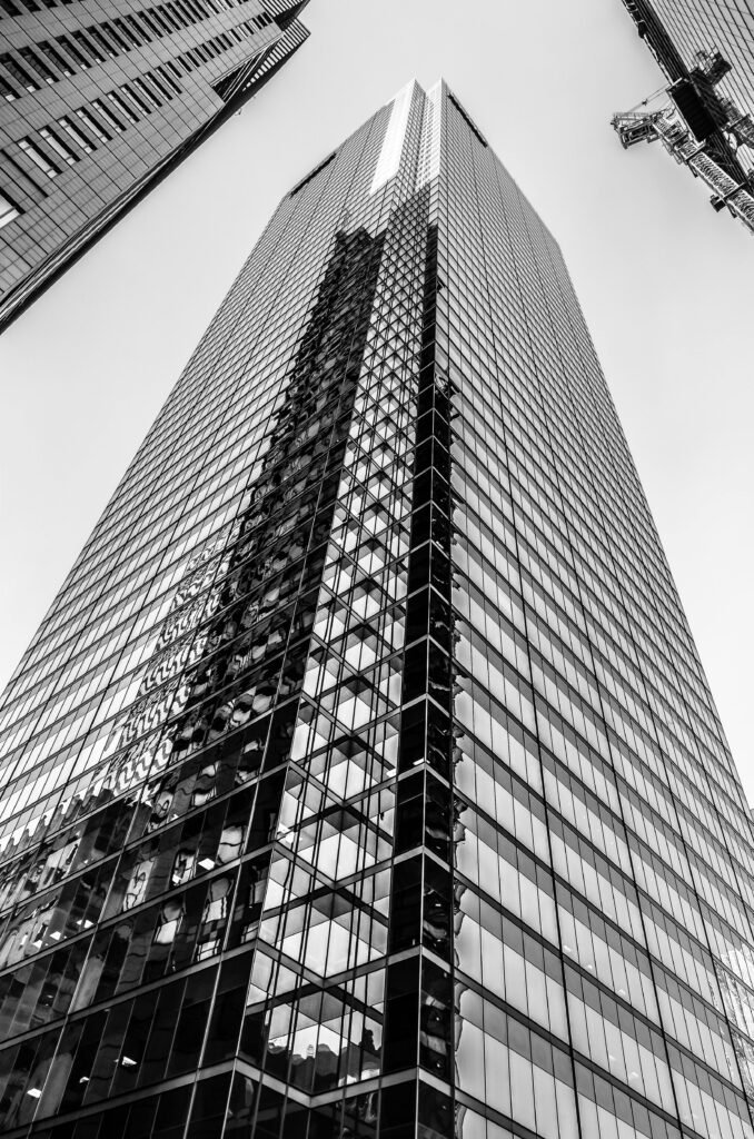 pexels photo 1697159 1697159 Low angle black and white view of a modern skyscraper with reflective glass facade and surrounding buildings.